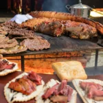 Auf dem Bild ist ein Tisch mit verschiedenen uruguayischen Gerichten zu sehen. Im Vordergrund befindet sich ein großes Asado, das aus verschiedenen Fleischsorten besteht. Das Fleisch ist über einem offenen Holzfeuer gegrillt und hat eine schöne braune Kruste. Neben dem Asado befinden sich noch weitere Gerichte auf dem Tisch, darunter Empanadas, Chivitos und Pastelitos. Die Empanadas sind gefüllte Teigtaschen, die mit Rindfleisch, Käse oder Gemüse gefüllt sein können. Die Chivitos sind Sandwiches, die mit Rindfleisch, Käse, Speck, Ei und Avocado belegt sind. Die Pastelitos sind süße Teigtaschen, die mit Marmelade, Käse oder Dulce de leche gefüllt sind. Das Bild vermittelt einen guten Eindruck von der Vielfalt der uruguayischen Küche. Es zeigt, dass die uruguayische Küche sowohl herzhafte als auch süße Gerichte bietet. Die Gerichte sind geprägt von europäischen und südamerikanischen Einflüssen und sind ein Genuss für jeden Gaumen.